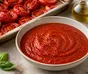 Cuenco de salsa de tomate roja y lisa, rodeado de tomates asados, ajo y albahaca