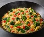 Sartén oscura con arroz frito, trozos de huevo, espinacas, brócoli, pimiento rojo, zanahoria y tirabeques